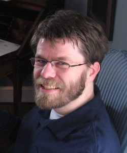 Photo of Alexander Benjamin Craghead, wearing a blue shirt and eyeglasses.